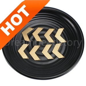 Może przedstawiać: Zbliżenie na dziewięć złotych metalowych zawieszek w kształcie strzałek na czarnym tle. Zawieszki mają około 2,5 cm długości i zakończone są ostrym grotem.