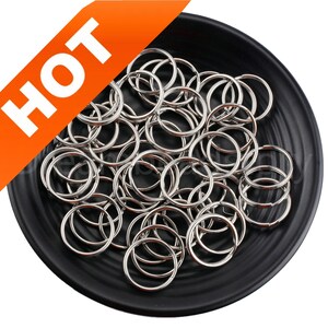 May include: A black dish filled with a large quantity of silver key rings. The key rings are all the same size and shape, and they are arranged in a random pattern.