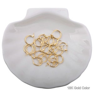 May include: A pile of gold-colored hoop earrings on a white seashell-shaped dish. 18K Gold Color.