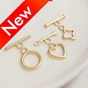 Puede incluir: Cuatro cierres de palanca de metal dorado con diferentes dijes: un círculo, un corazón, una flecha y una estrella.