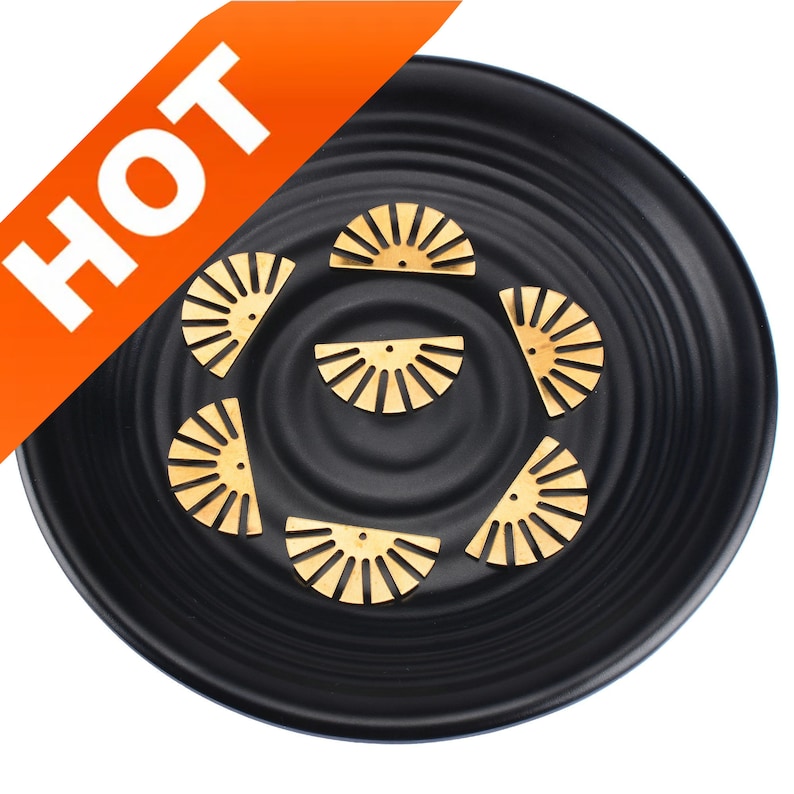May include: A set of six gold-colored metal half-circle charms with a sunburst design. The charms are arranged on a black plate.