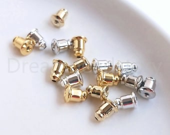 May include: A close-up of a group of gold and silver earring backs. The backs are small and round, with a post that fits into the hole in an earring.
