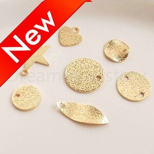 Könnte beinhalten: Ein Set aus sieben goldfarbenen Metall-Anhängern in verschiedenen Formen, darunter ein Stern, ein Herz, ein Blatt und Kreise. Die Anhänger haben eine strukturierte Oberfläche und ein Loch zum Anbringen an Schmuck oder anderen Bastelarbeiten.