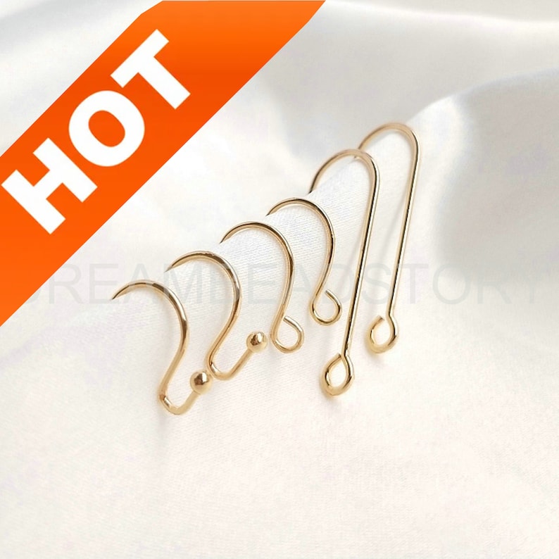 May include: Five gold earring hooks with a small ball at the end of each hook. The hooks are arranged in a row, with the largest hook on the left and the smallest hook on the right.