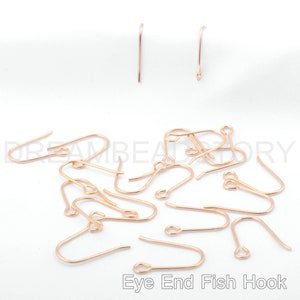 May include: A close-up of a pile of gold-toned eye end fish hook earring findings. The hooks are made of metal and have a small loop at the top for attaching to earrings.