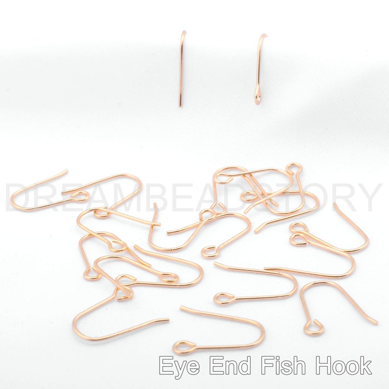 May include: A close-up of a pile of gold-toned eye end fish hook earring findings. The hooks are made of metal and have a small loop at the top for attaching to earrings.