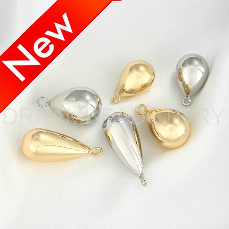 Peut inclure: Six breloques en m&eacute;tal en forme de goutte d'eau, en argent et en or. Les breloques ont une boucle en haut pour les attacher &agrave; des bijoux.
