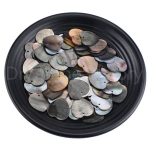 May include: A black bowl filled with a large quantity of heart-shaped mother of pearl shell beads. The beads are a mix of black, brown, and white colours with iridescent shimmer.