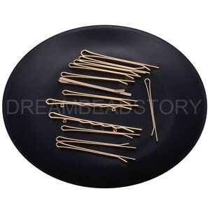May include: A set of 15 gold hair clips on a black plate. The clips are various sizes and shapes, with some having a wavy design.