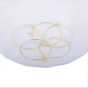 May include: Four gold-coloured hoop earrings on a white surface. The hoops are simple and circular.