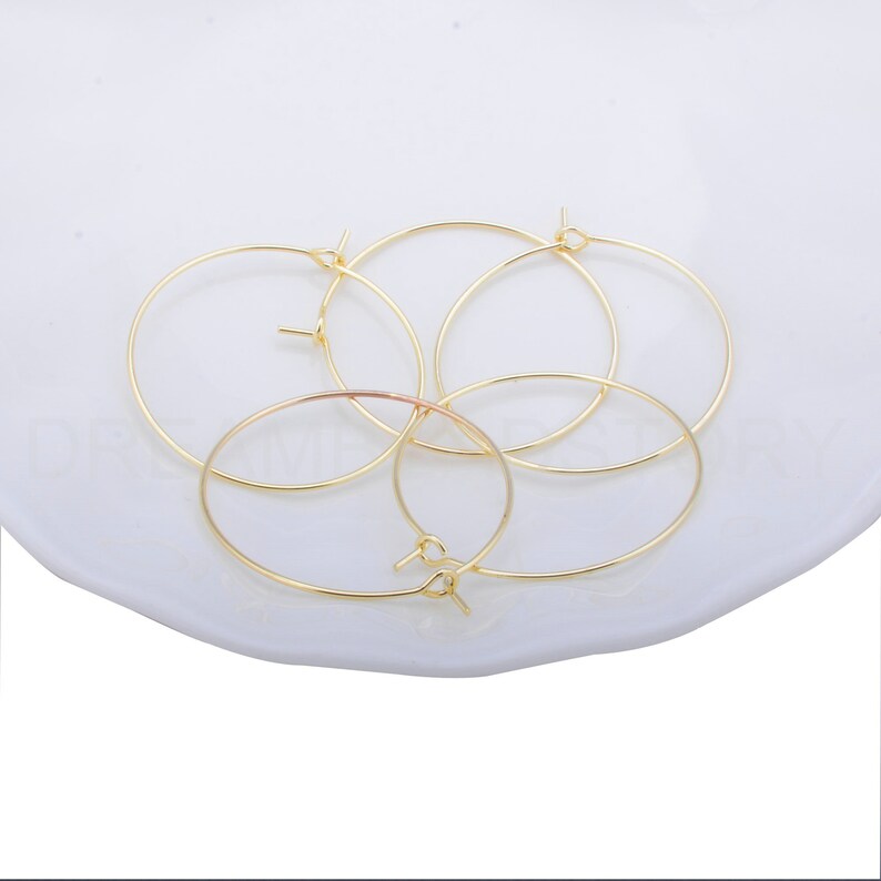 May include: Four gold-coloured hoop earrings on a white surface. The hoops are simple and circular.