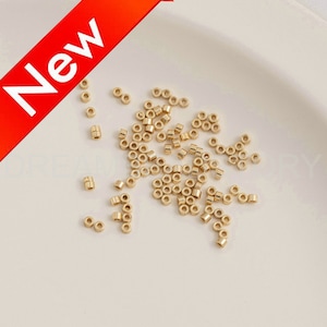 May include: A close-up of a pile of small, gold-colored metal rings. The rings are about 4mm in diameter and are scattered on a white surface.