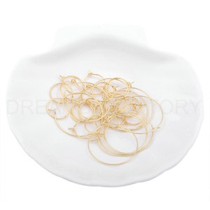 May include: A pile of gold-toned hoop earrings on a white surface.
