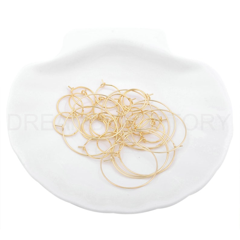 May include: A pile of gold-toned hoop earrings on a white surface.