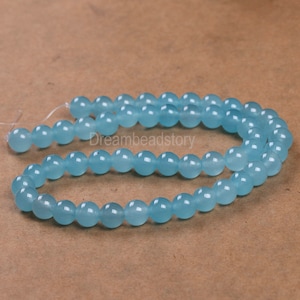 May include: A strand of light blue round beads made of jade. The beads are smooth and polished.