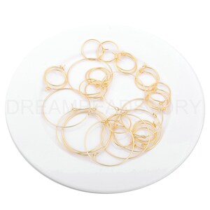 May include: A pile of gold-coloured hoop earrings on a white plate. The earrings are various sizes and are made of thin metal.