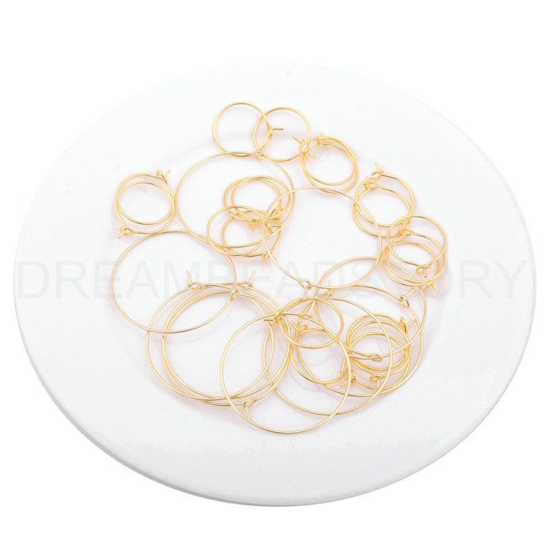 May include: A pile of gold-coloured hoop earrings on a white plate. The earrings are various sizes and are made of thin metal.