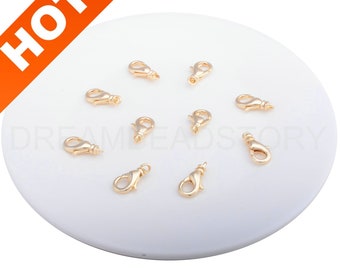 May include: Ten gold-toned lobster clasps on a white surface. The clasps are a common jewelry finding used for necklaces, bracelets, and other jewelry projects.
