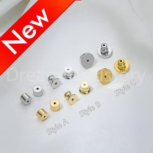 Puede incluir: Una variedad de cierres de pendientes en tonos plateados y dorados. La imagen muestra varios estilos, incluyendo respaldos cilíndricos y en forma de disco, etiquetados como Estilo A, B y C. Una pancarta roja con la palabra "Nuevo" está en la esquina superior izquierda.