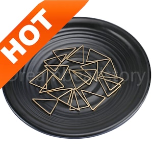 May include: A black plate with a pile of gold triangle shaped metal charms. The charms are about 2.5 cm in size.