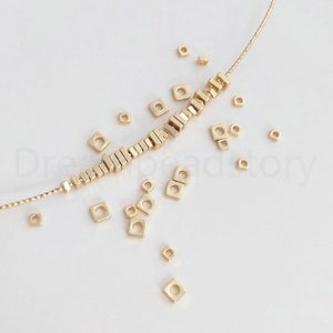 Pu&ograve; includere: Perle quadrate dorate infilate su una collana a catena. Le perle sono sparse intorno alla collana, creando un motivo decorativo.