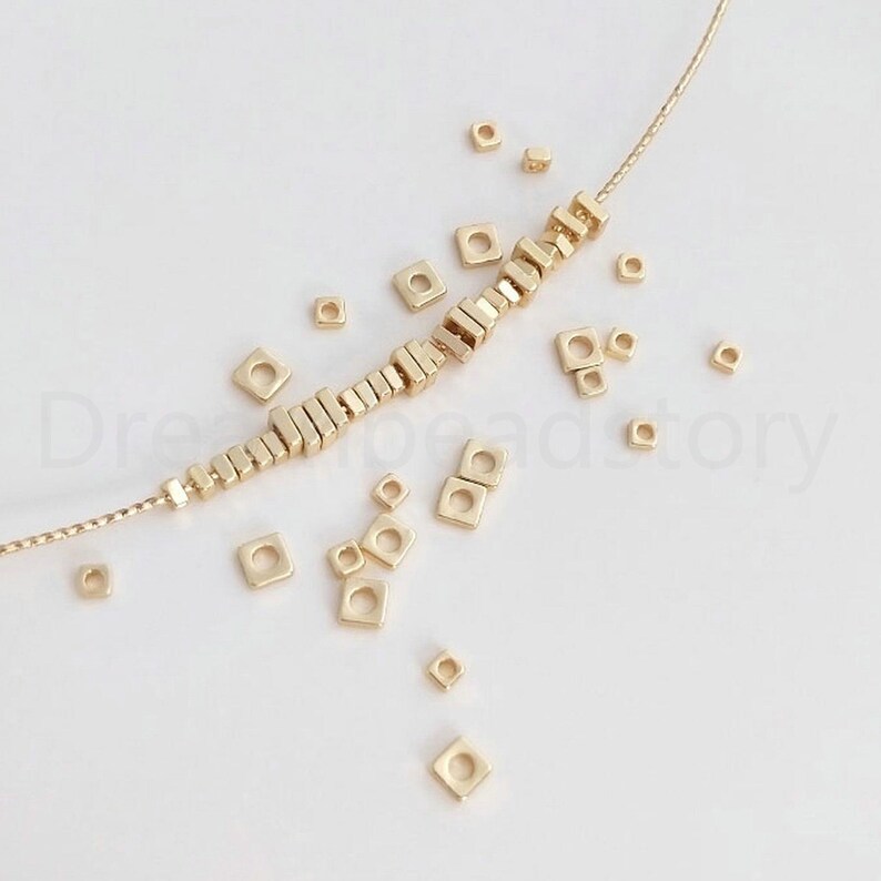 Pu&ograve; includere: Perle quadrate dorate infilate su una collana a catena. Le perle sono sparse intorno alla collana, creando un motivo decorativo.