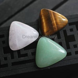 Puede incluir: Tres cabujones triangulares, uno verde claro, uno blanco y uno marrón con patrón de ojo de tigre.