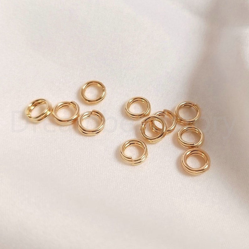 以下が含まれることがあります： 金色のジャンプリングのグループのクローズアップ。リングは小さく繊細で、ジュエリー作りに最適です。