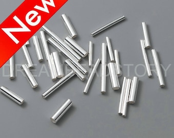 Può includere: Un gruppo di tubi metallici color argento, sparsi su una superficie grigia. I tubi sono di diverse lunghezze e sono tutti lisci e lucidi.