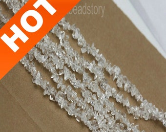 May include: A strand of clear quartz crystal chips, also known as rock crystal, arranged in rows on a brown surface. The chips are irregular in shape and size, with some having a slightly frosted appearance. The image is labeled "HOT" in a red and orange banner.