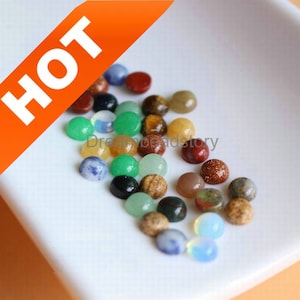 Op de afbeelding: Assortiment van ronde cabochon edelstenen in verschillende kleuren, waaronder groen, blauw, rood, bruin en geel. De edelstenen zijn ongeveer 10 mm in diameter en zijn ideaal voor het maken van sieraden.