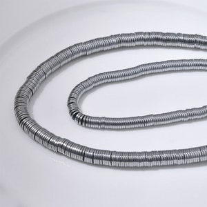 Pu&ograve; includere: Una collana di perline in metallo color argento, ogni perlina &egrave; un cerchio piatto con un bordo leggermente rialzato. Le perline sono infilate insieme per formare una lunga collana.