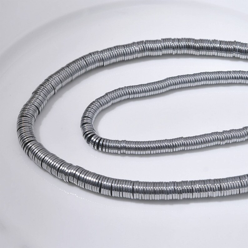 Pu&ograve; includere: Una collana di perline in metallo color argento, ogni perlina &egrave; un cerchio piatto con un bordo leggermente rialzato. Le perline sono infilate insieme per formare una lunga collana.