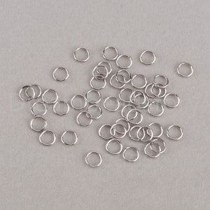 May include: A large pile of silver jump rings, a type of jewelry finding used for connecting chains, cords, and other jewelry components.