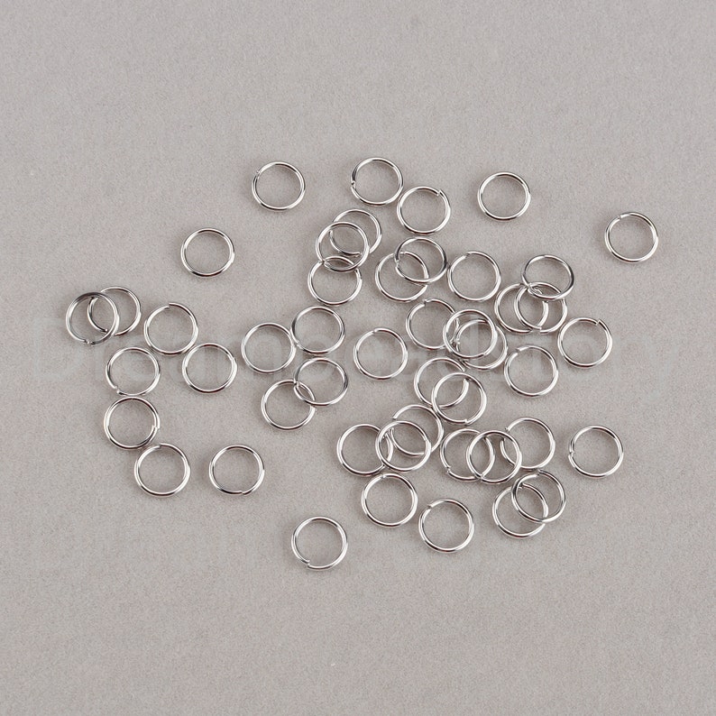 May include: A large pile of silver jump rings, a type of jewelry finding used for connecting chains, cords, and other jewelry components.
