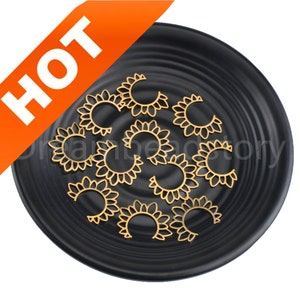 May include: Gold-coloured, open-work metal charms in a half-sunflower design are scattered on a black plate. The word "HOT" is displayed in white letters on an orange banner in the upper left corner. The charms are likely for jewellery making.