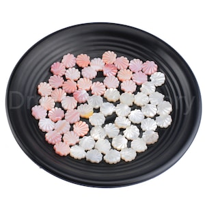 May include: A collection of white and pink shell flower shapes on a black plate. The shell shapes are all approximately the same size and have a delicate, scalloped edge.
