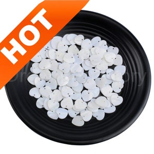 May include: A black plate filled with white heart-shaped shell beads. The beads have a hole in the center for stringing.