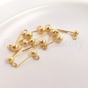 Puede incluir: Un grupo de hallazgos de pendientes de color dorado con una bola texturizada en el extremo de cada hallazgo. Los hallazgos tienen un bucle en la parte superior para sujetar a las joyas.