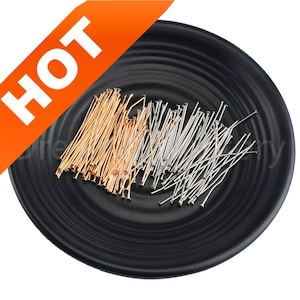 May include: A black dish filled with a large quantity of gold and silver head pins. The pins are arranged in a random pattern.