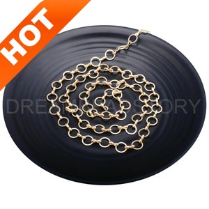 Puede incluir: Un collar de cadena dorada con un delicado diseño de eslabones redondos. La cadena está enrollada en un plato negro.