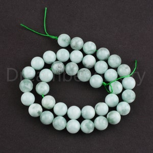 Peut inclure: Un collier de perles de jade vert clair, chaque perle est ronde et lisse. Les perles sont enfilées sur un fil vert.