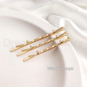 May include: Three gold wavy hair clips with two loops at the end of each clip. The clips are arranged in a row, with the top clip slightly offset from the others. The text "Wavy 2 Loops" is printed below the clips.
