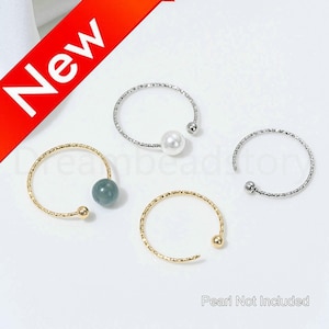 May include: Four open-ended rings in gold and silver tones, each with a decorative bead or pearl. One ring has a blue-green bead, another a white pearl, and two have small gold or silver balls. The word "New" is in a red banner.