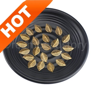 May include: A black plate with 20 gold metal leaf charms. The charms are in the shape of a leaf with a hole at the top.