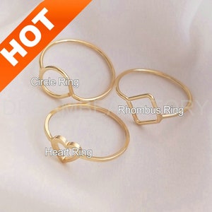May include: Three gold rings with different shapes: a circle, a heart, and a rhombus. The rings are on a white background.