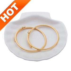 May include: Two gold-toned bangle bracelets with a twisted wire design. The bracelets are displayed on a white seashell-shaped dish.