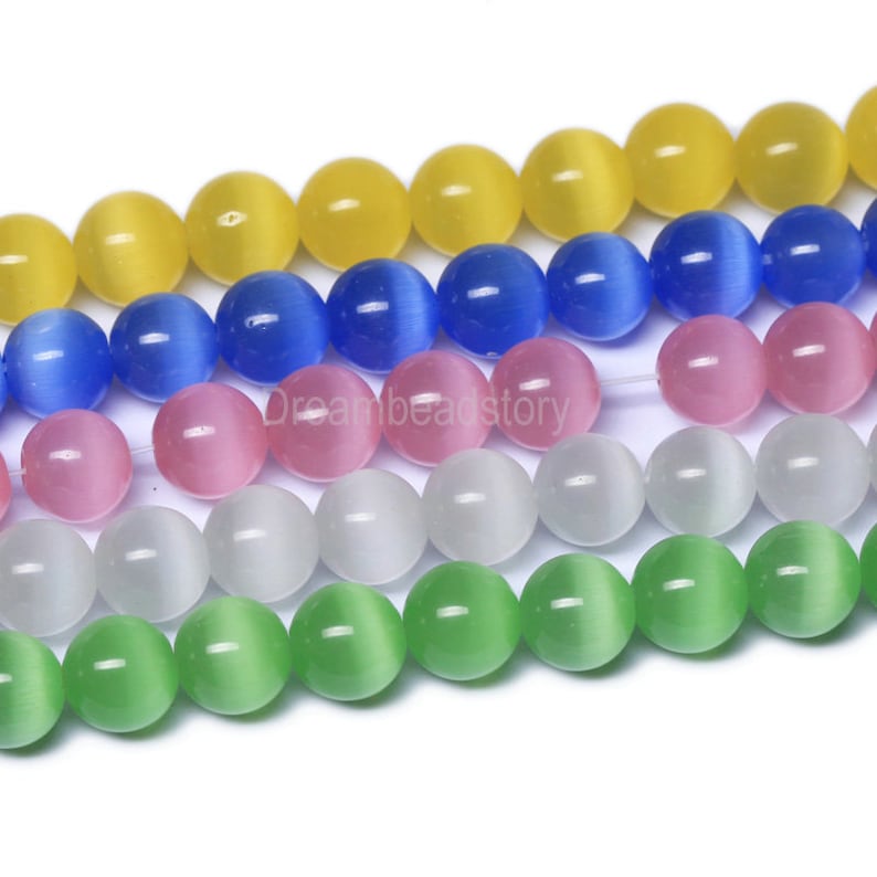 May include: A strand of round, iridescent glass beads in various colors, including yellow, blue, pink, white, and green. The beads have a cat's eye effect, with a shimmering line running through the center of each bead.