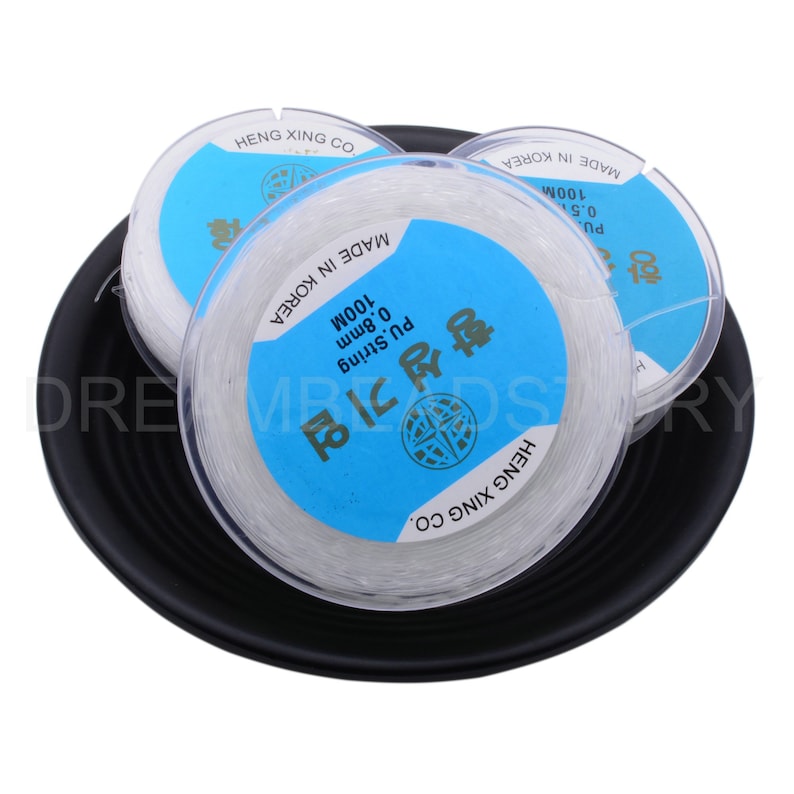 Puede incluir: Tres carretes de hilo el&aacute;stico transparente, cada uno con una etiqueta azul que dice "PU String 0.8mm 100M Made in Korea" y "HENG XING CO."