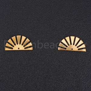 May include: Two gold-colored metal sunburst shapes with a hole in the center. The shapes are on a black background.